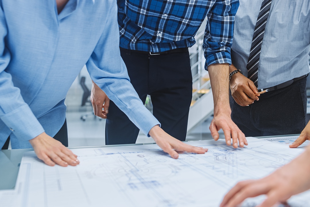 Professionals leaning over a table to review technical blueprints.