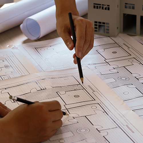 Close-up of two pairs of hands drawing on architectural blueprints.