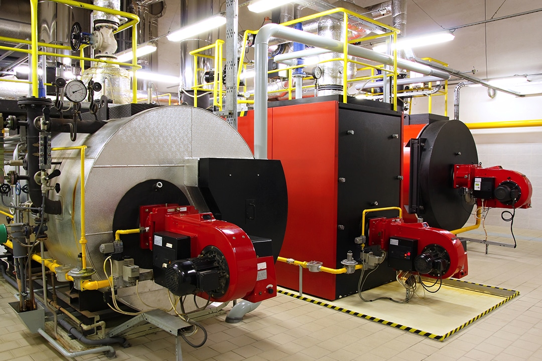 Industrial boiler room with large silver and red boiler units.