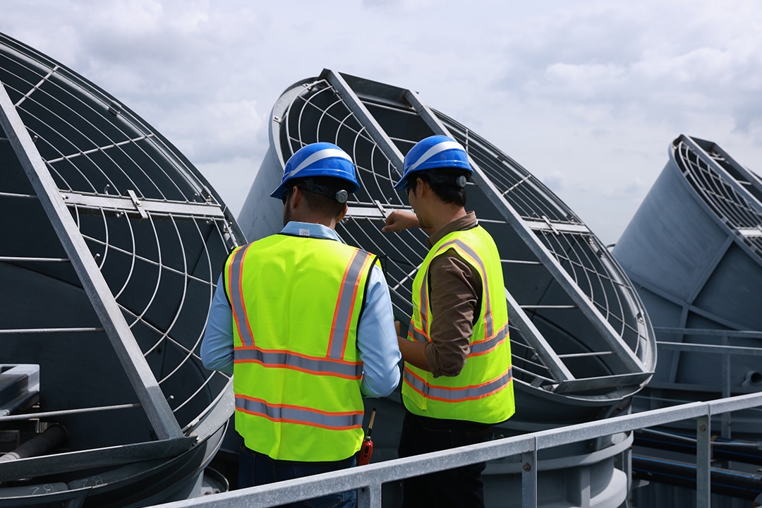 Two technicians inspecting large industrial cooling fans on a rooftop.