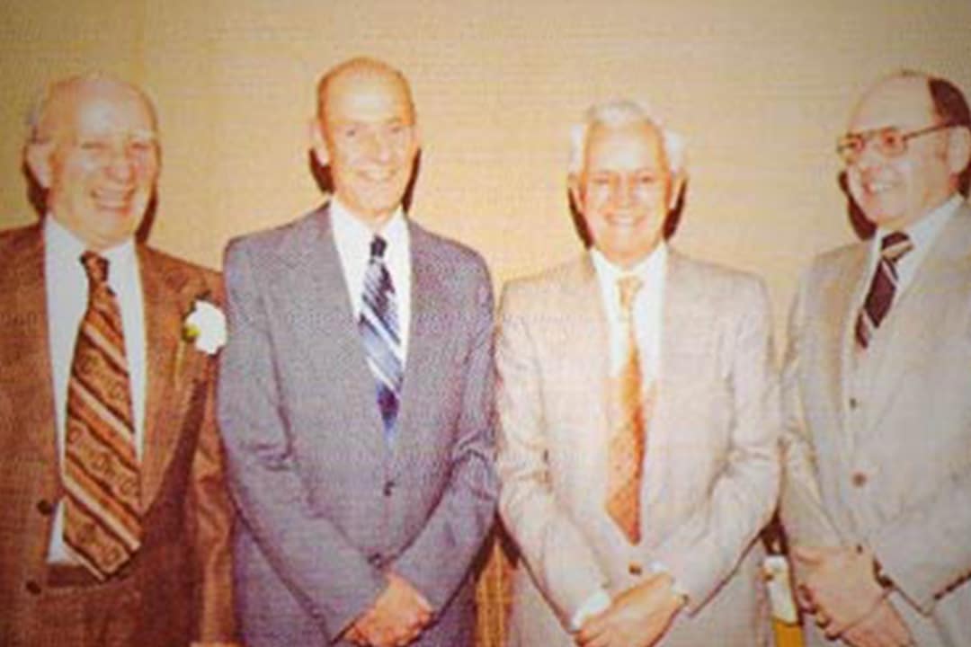 Four smiling business partners in suits from the 1970s.