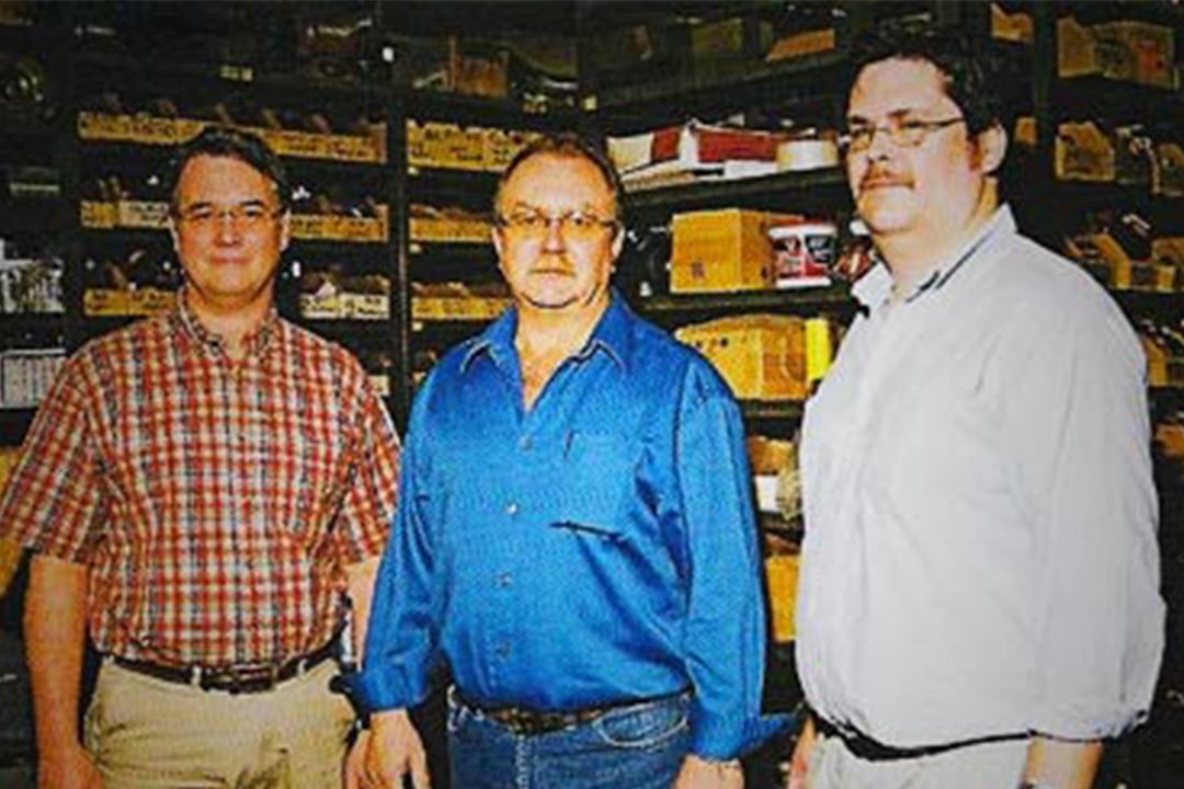 Three men standing in front of warehouse storage shelves.