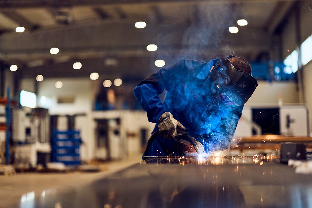 Professional welder welding metal with sparks in a workshop.