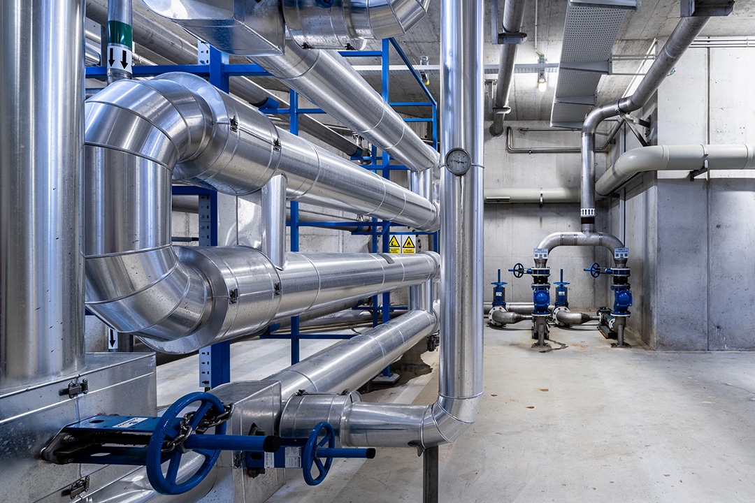 Insulated metallic pipes with blue valves in concrete room.