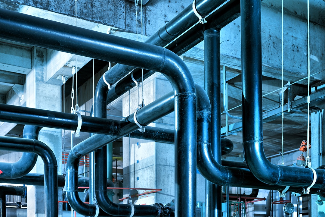 Network of black insulated pipes suspended from concrete ceiling.