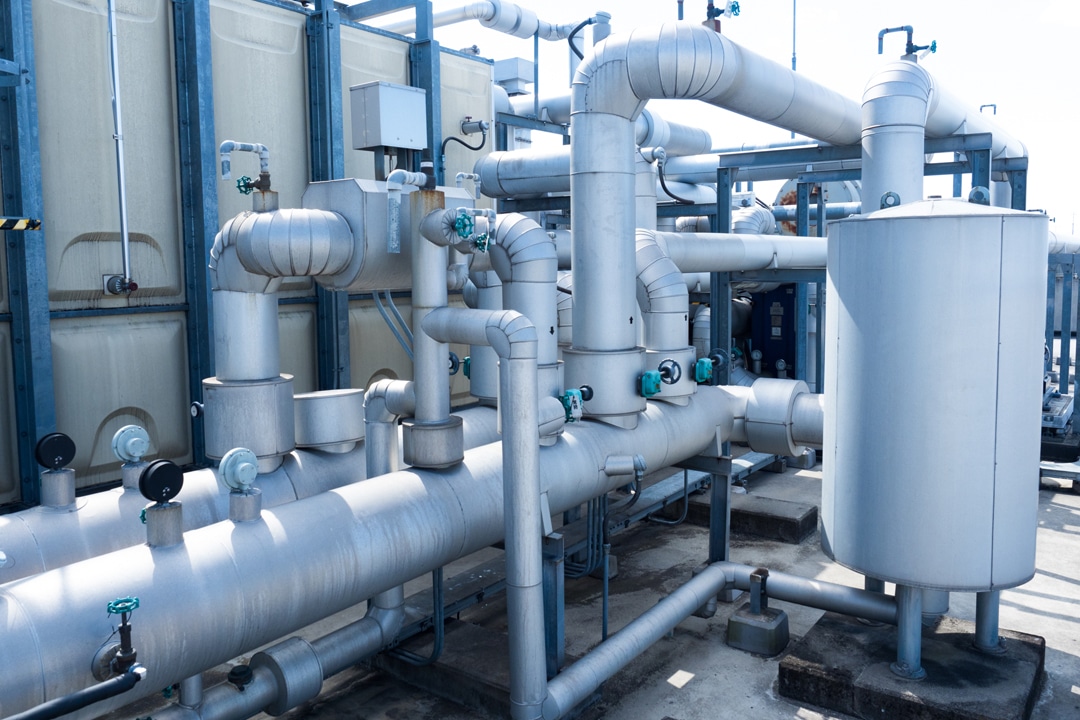 Industrial rooftop plumbing system with large insulated metal pipes.
