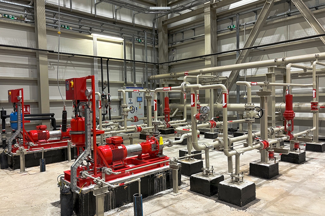 Industrial pump room featuring red motors and complex pipe systems.