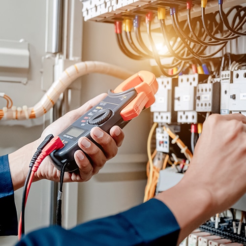Close-up of hands using a multimeter to test electrical panel wiring.